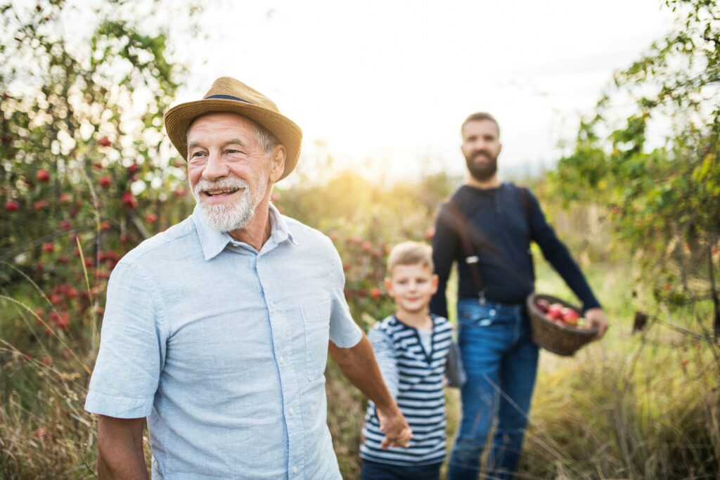 An intergenerational family pick apples in a sunkissed orchard, for “How to Use Alternative Investments for Retirement Income in a 401(k)”